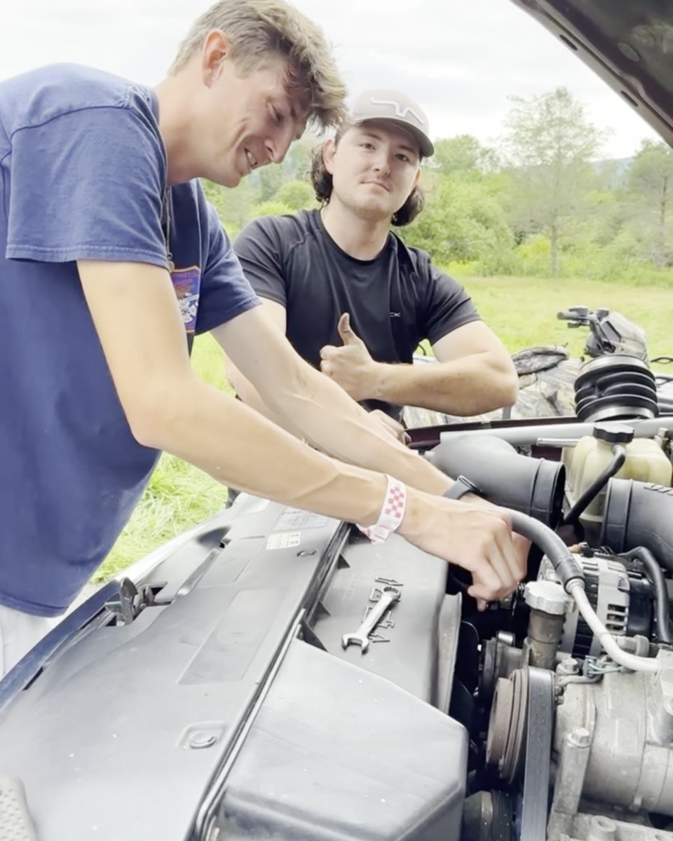Mason giving a thumbs up while a friend works under the hood